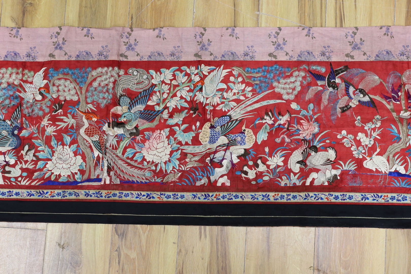 An early 20th century Chinese embroidered silk helmet multi coloured embroidery on a red background depicting oriental birds. 183cm x 47.5cm. 183cm x 47.5cm